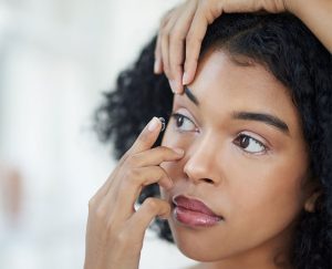 African American placing contact lense into her eye | Eyewear & Contact Lenses